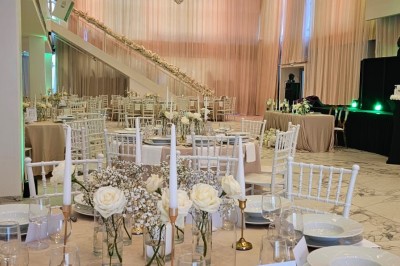 Salle extérieure aménagée avec des tables hautes noires, décorations florales blanches et lumière naturelle.