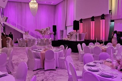 Salle extérieure aménagée avec des tables hautes noires, décorations florales blanches et lumière naturelle.