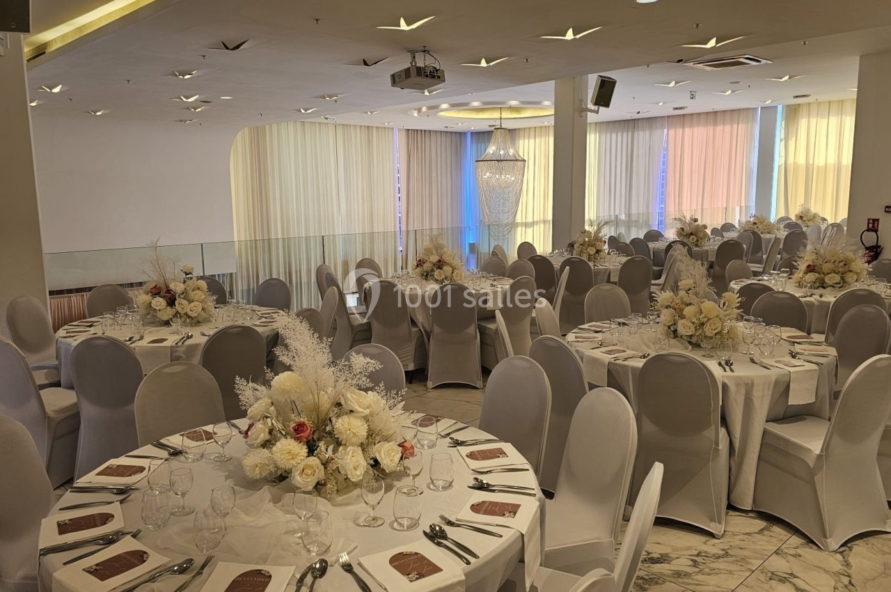 Salle de réception élégante avec tables rondes dressées, nappes blanches et décorations florales raffinées.