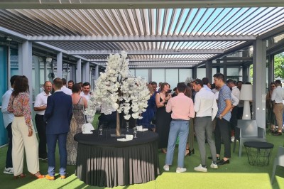 Salle extérieure aménagée avec des tables hautes noires, décorations florales blanches et lumière naturelle.