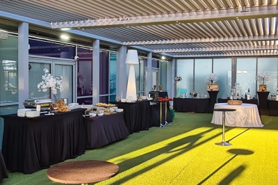 Salle extérieure aménagée avec des tables hautes noires, décorations florales blanches et lumière naturelle.