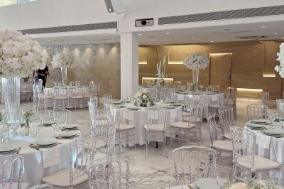 Salle extérieure aménagée avec des tables hautes noires, décorations florales blanches et lumière naturelle.
