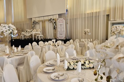 Salle extérieure aménagée avec des tables hautes noires, décorations florales blanches et lumière naturelle.