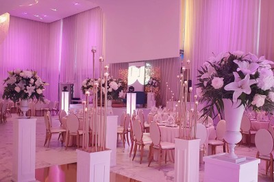 Salle extérieure aménagée avec des tables hautes noires, décorations florales blanches et lumière naturelle.