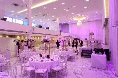 Salle extérieure aménagée avec des tables hautes noires, décorations florales blanches et lumière naturelle.