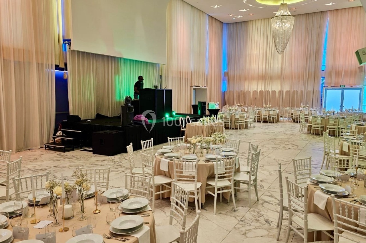 Salle de réception élégante avec tables dressées, chaises blanches et scène équipée pour un événement.