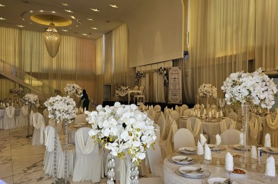 Salle extérieure aménagée avec des tables hautes noires, décorations florales blanches et lumière naturelle.