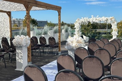 Salle extérieure aménagée avec des tables hautes noires, décorations florales blanches et lumière naturelle.