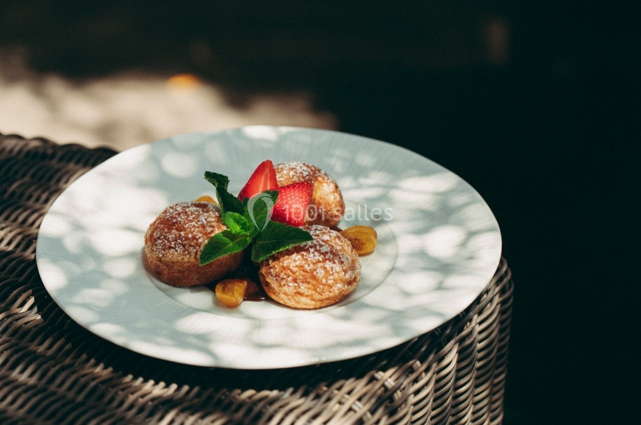 Assiette de beignets saupoudrés de sucre glace, garnis de fraises, feuilles de menthe et accompagnés de morceaux de fruits.
