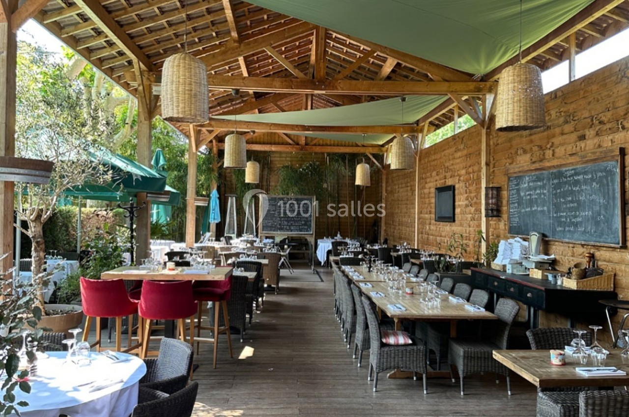 Salle de restaurant en terrasse couverte avec tables dressées, mobilier en bois et ambiance chaleureuse.