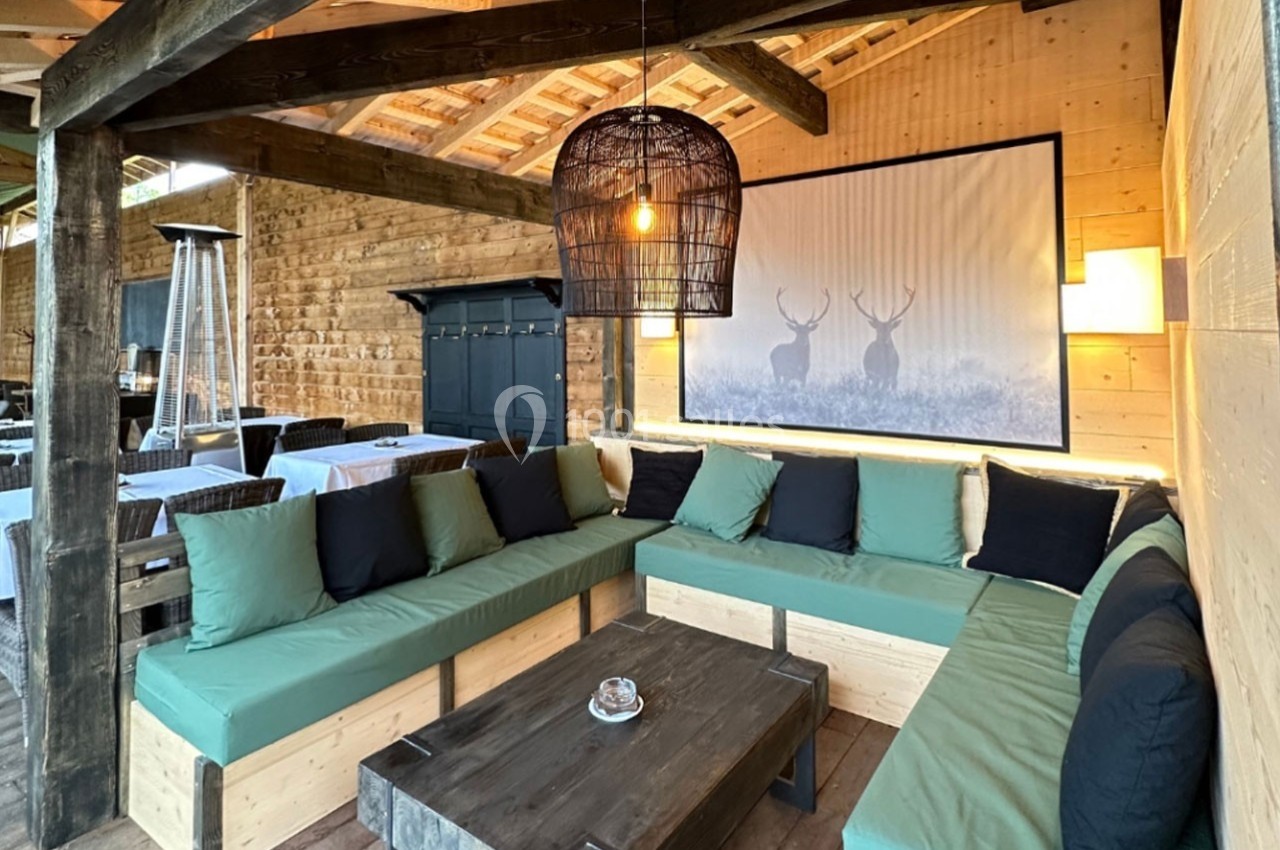 Salon extérieur en bois avec banquettes vertes, table basse et décoration murale représentant des cerfs.