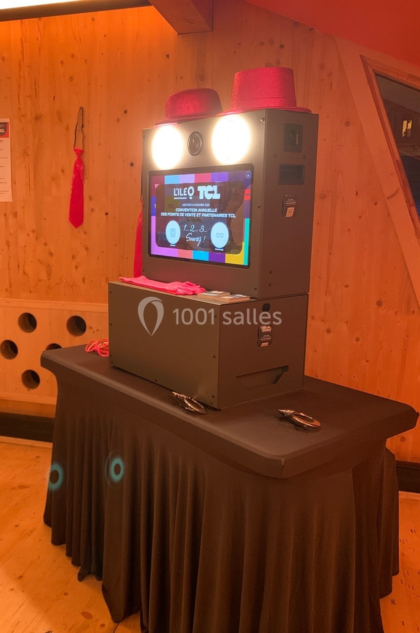 Borne photo interactive sur une table noire, entourée de décorations rouges dans un espace en bois.