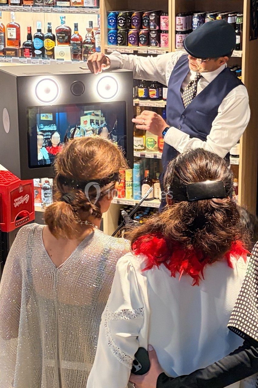 Un homme présente une borne photo interactive à trois femmes dans un magasin rempli de bouteilles d'alcool.