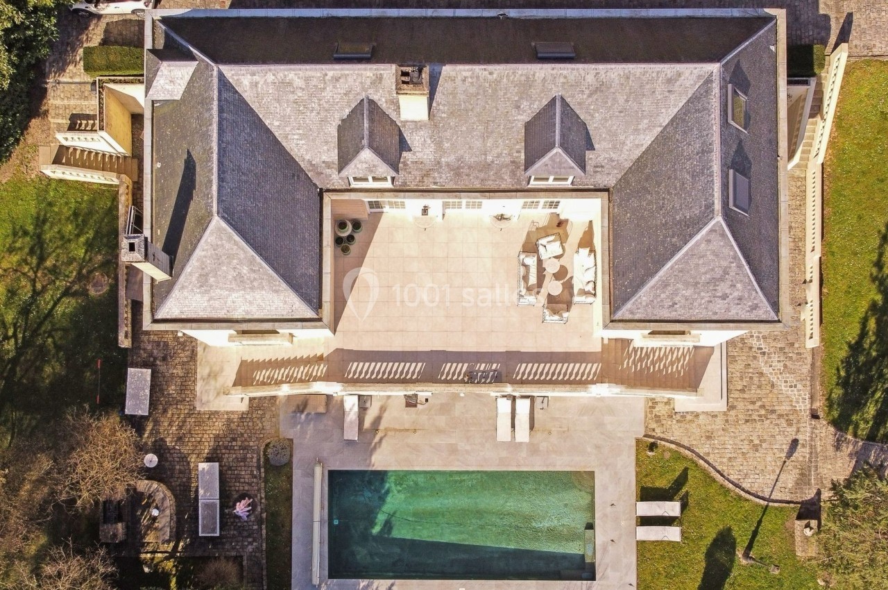 Vue aérienne d'une maison avec terrasse, piscine rectangulaire et jardin environnant.