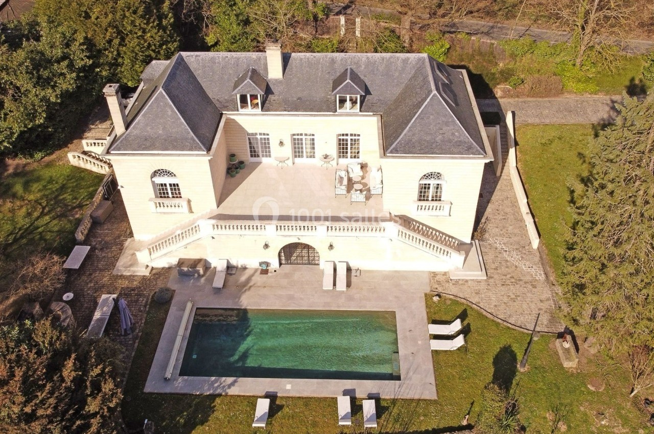 Vue aérienne d'une maison en pierre avec toit en ardoise, terrasse spacieuse et piscine entourée de verdure.