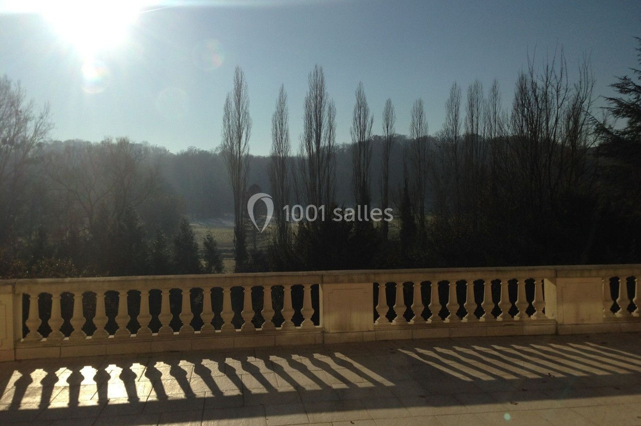 Terrasse ensoleillée avec balustrade, ombres marquées et vue sur des arbres en hiver sous un ciel dégagé.