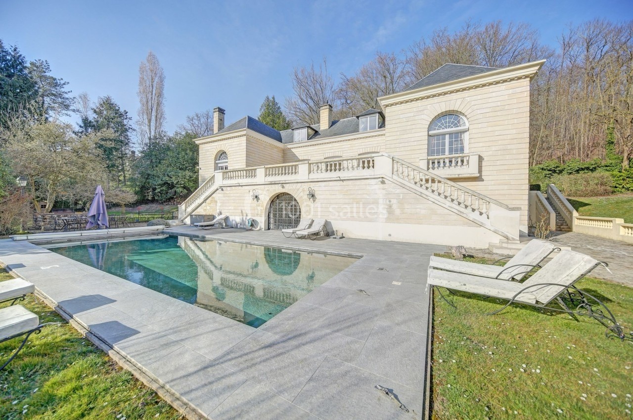 Grande maison en pierre avec piscine extérieure, entourée de verdure et située dans un cadre arboré.