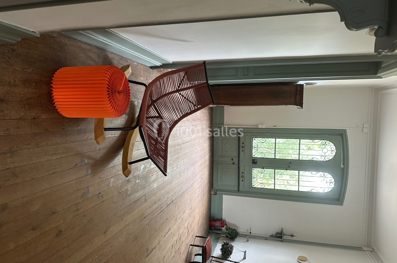 Chaise design en bois et métal rouge avec un tabouret orange, posés sur un parquet dans une pièce lumineuse.