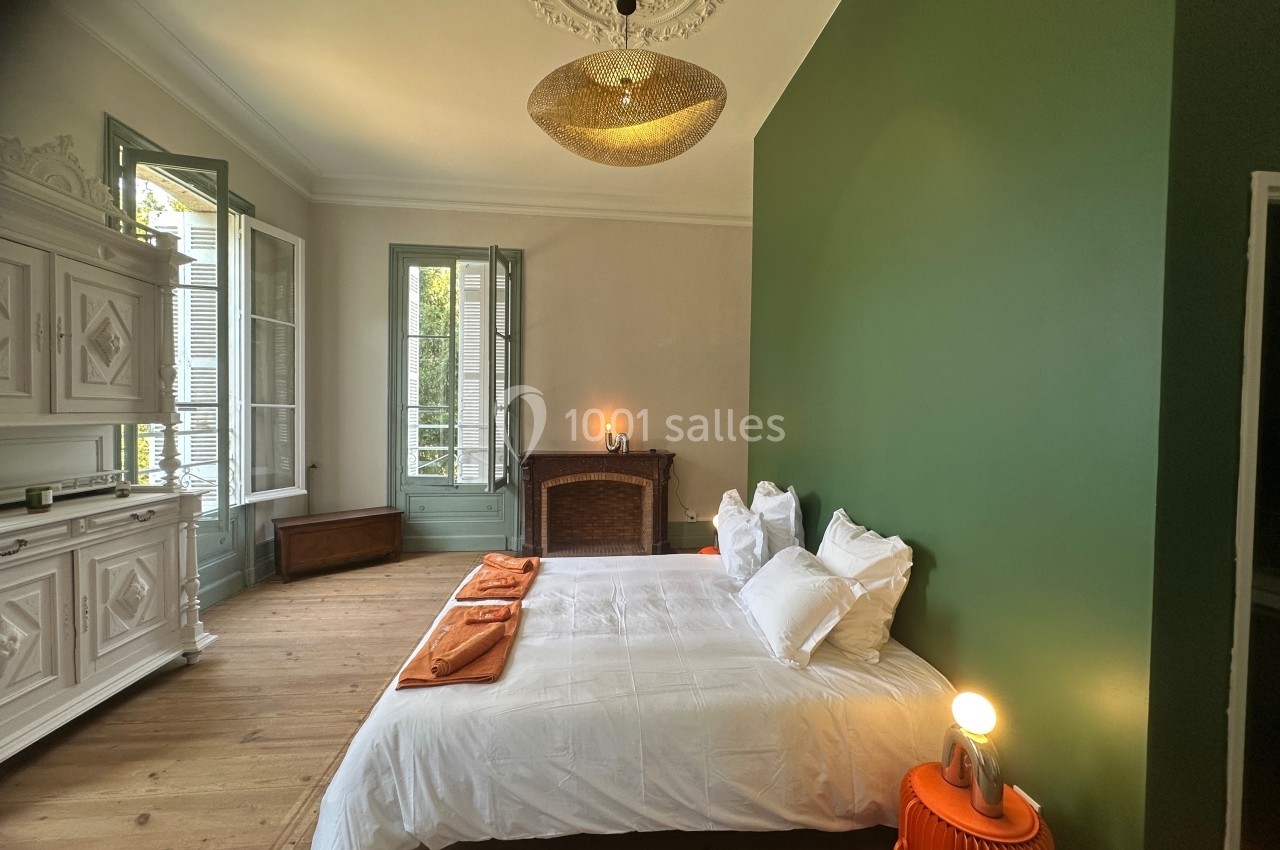 Chambre lumineuse avec murs verts et blancs, lit double, mobilier ancien, grandes fenêtres et parquet en bois.