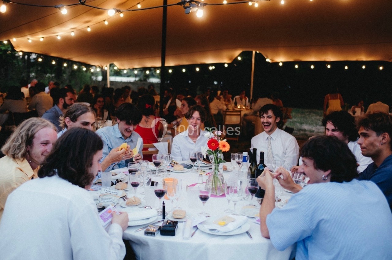 Groupe de personnes assises autour d'une table lors d'un dîner en extérieur sous une tente éclairée.