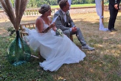Miniature cérémonie laïque Un couple en tenue de mariage marche dans une salle en briques, avec un bouquet de fleurs au premier plan.