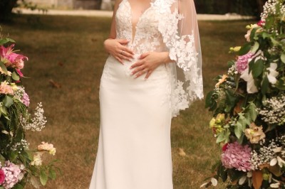 Miniature cérémonie laïque Un couple en tenue de mariage marche dans une salle en briques, avec un bouquet de fleurs au premier plan.