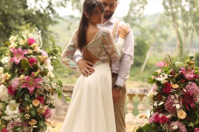 Miniature cérémonie laïque Un couple en tenue de mariage marche dans une salle en briques, avec un bouquet de fleurs au premier plan.