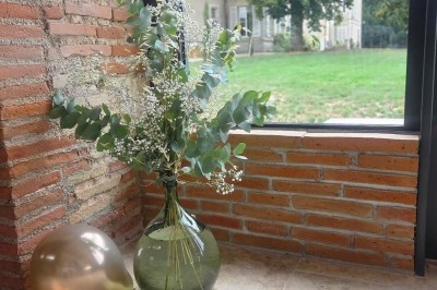 Miniature décoration Un couple en tenue de mariage marche dans une salle en briques, avec un bouquet de fleurs au premier plan.
