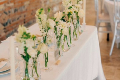 Miniature décoration de table Un couple en tenue de mariage marche dans une salle en briques, avec un bouquet de fleurs au premier plan.