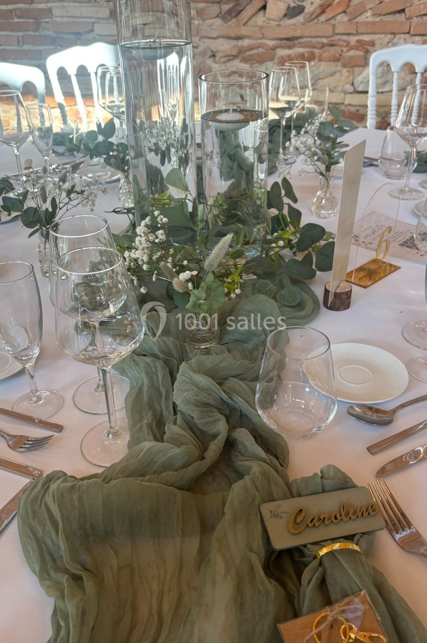 Table décorée pour un événement avec chemin de table vert, verres, couverts, bougies et compositions florales.
