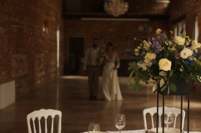 Miniature la salle de réception Un couple en tenue de mariage marche dans une salle en briques, avec un bouquet de fleurs au premier plan.