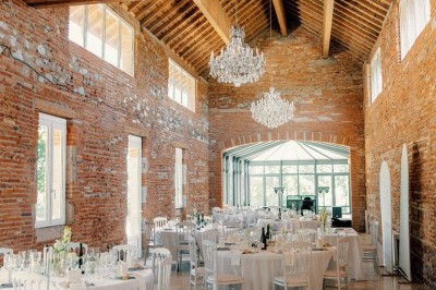 Miniature la salle de réception Un couple en tenue de mariage marche dans une salle en briques, avec un bouquet de fleurs au premier plan.