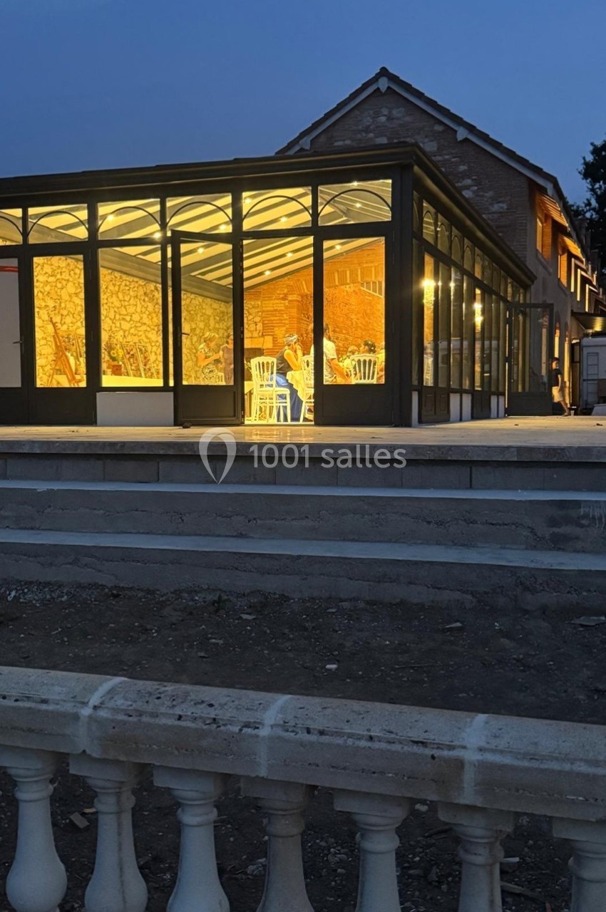 Véranda éclairée en soirée, attenante à une maison en rénovation, avec des chaises visibles à l'intérieur.
