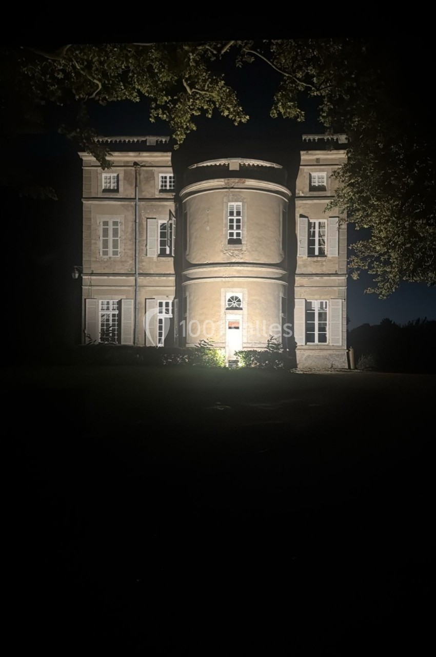 Façade éclairée d'un bâtiment ancien à trois étages, entouré d'arbres, photographié de nuit.
