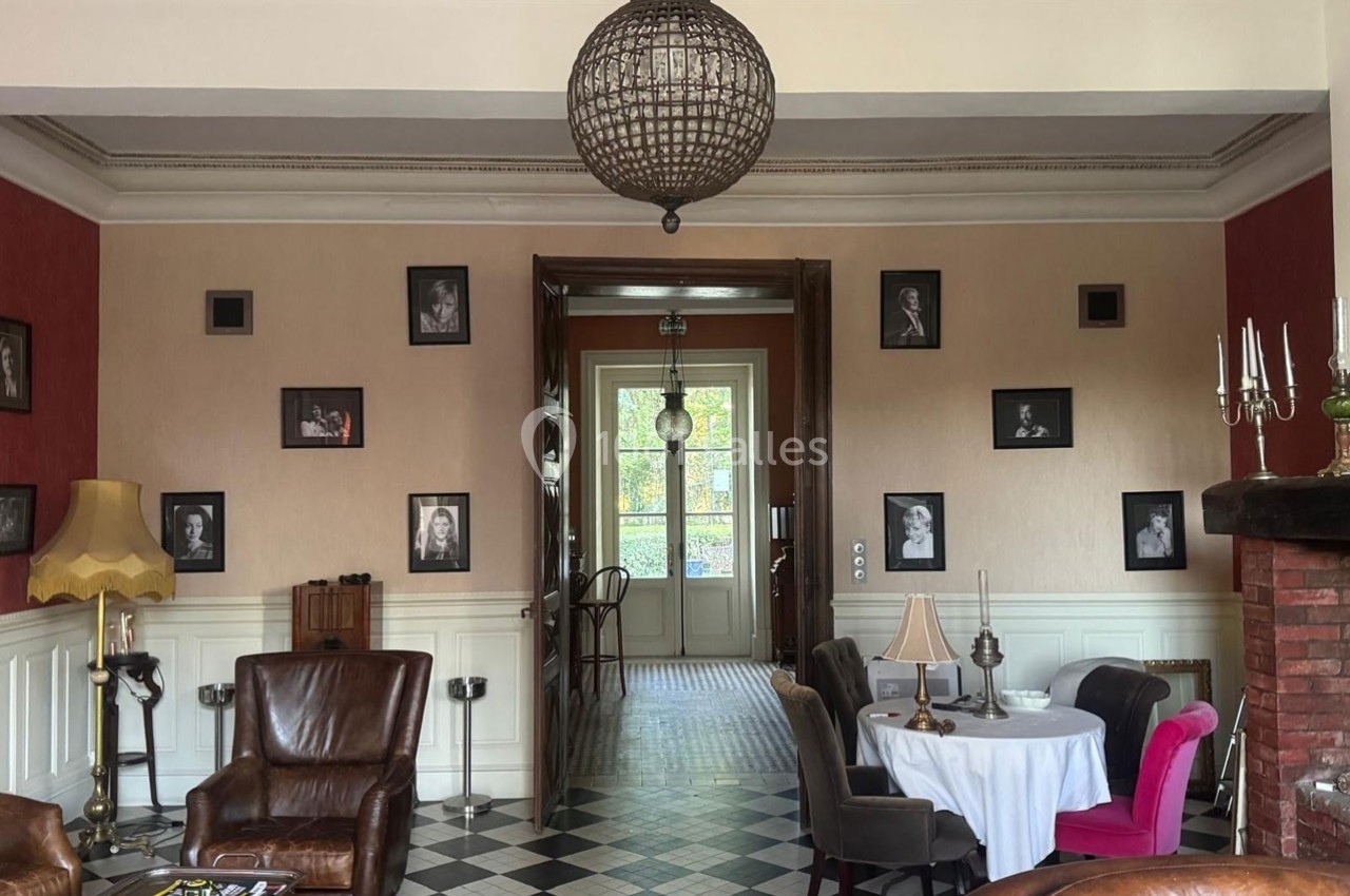Salon élégant avec fauteuils en cuir, table ronde, cheminée et murs décorés de portraits en noir et blanc.