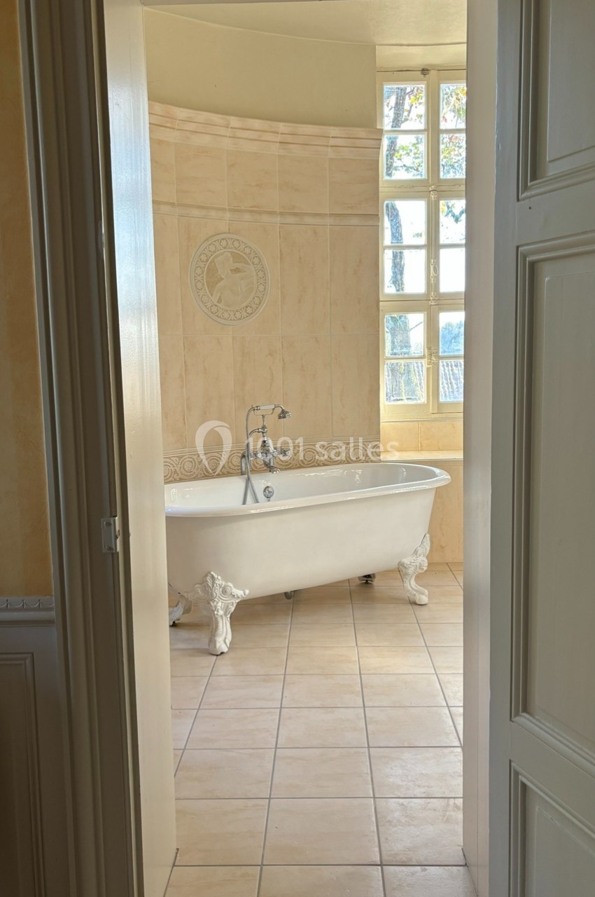Salle de bain lumineuse avec une baignoire sur pieds, carrelage beige et fenêtre à carreaux laissant entrer la lumière.