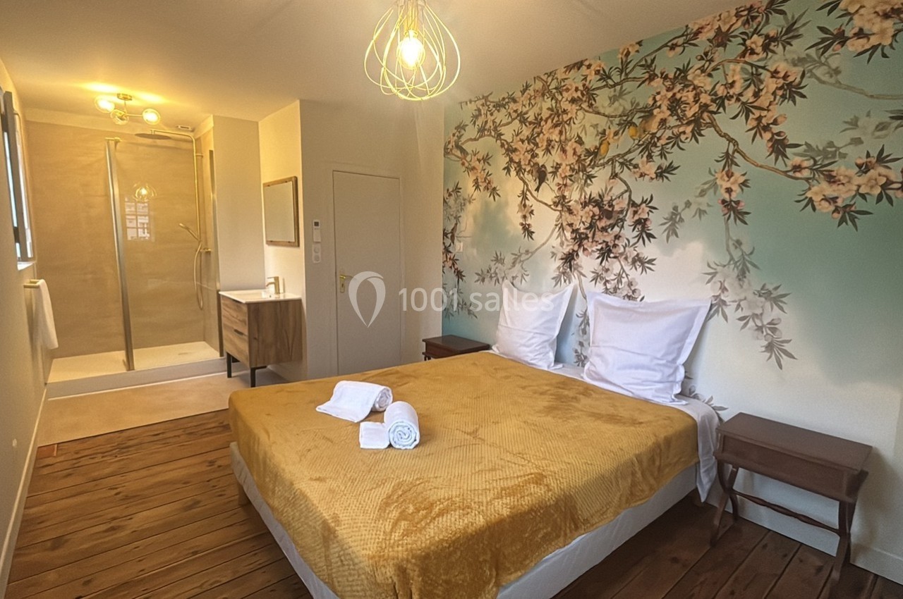 Chambre lumineuse avec lit double, linge de lit jaune, mur décoré de motifs floraux et salle de bain attenante.