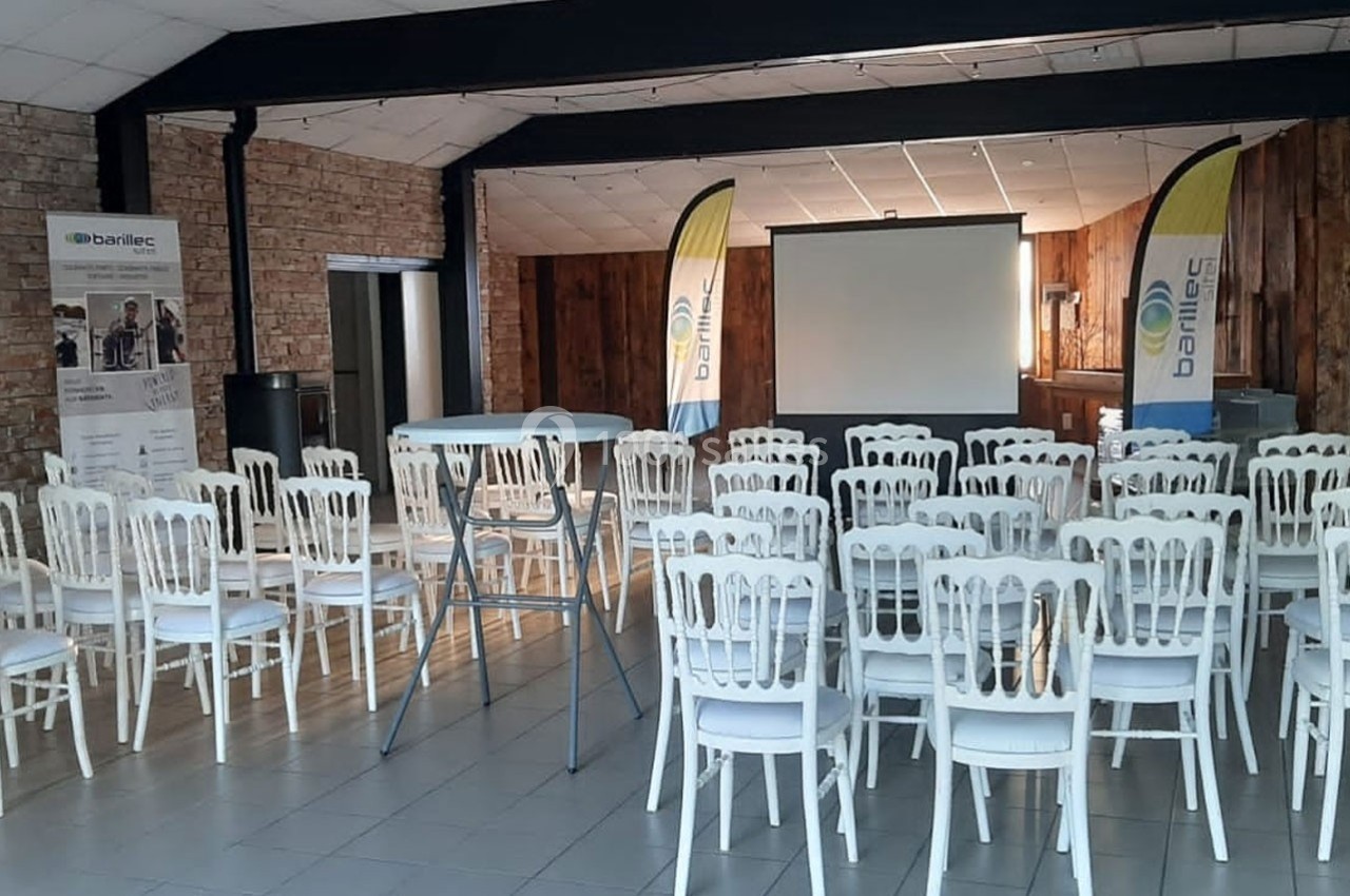 Salle de conférence avec des chaises blanches alignées, un écran de projection et des kakémonos en arrière-plan.
