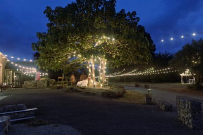 Façade d'un bâtiment moderne avec une table dressée sous un parasol rouge, entourée de décorations lumineuses.