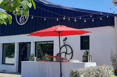 Façade d'un bâtiment moderne avec une table dressée sous un parasol rouge, entourée de décorations lumineuses.