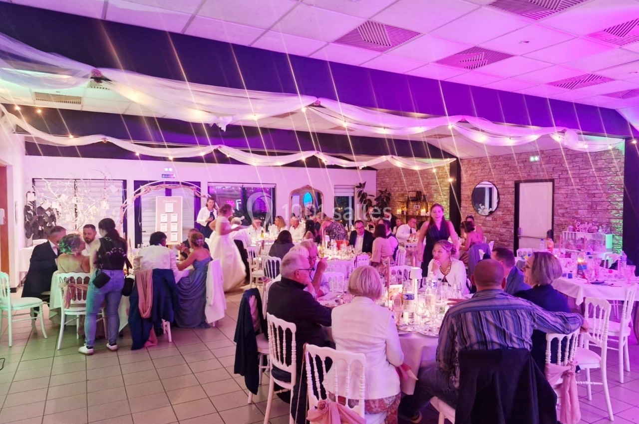 Salle de réception décorée, avec des invités assis à des tables rondes et une ambiance lumineuse festive.