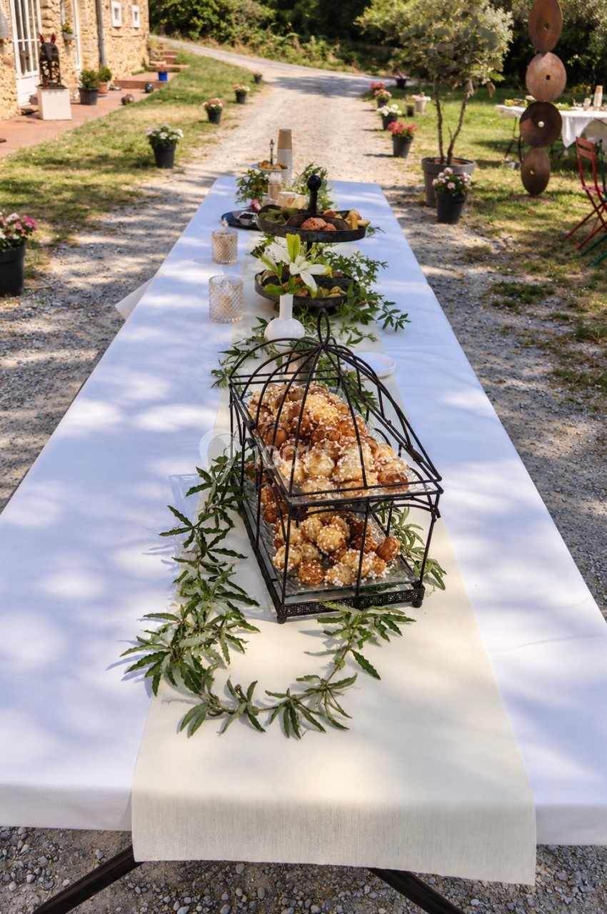 Table extérieure décorée pour un événement, avec nappes blanches, compositions florales et éléments décoratifs rustiques.