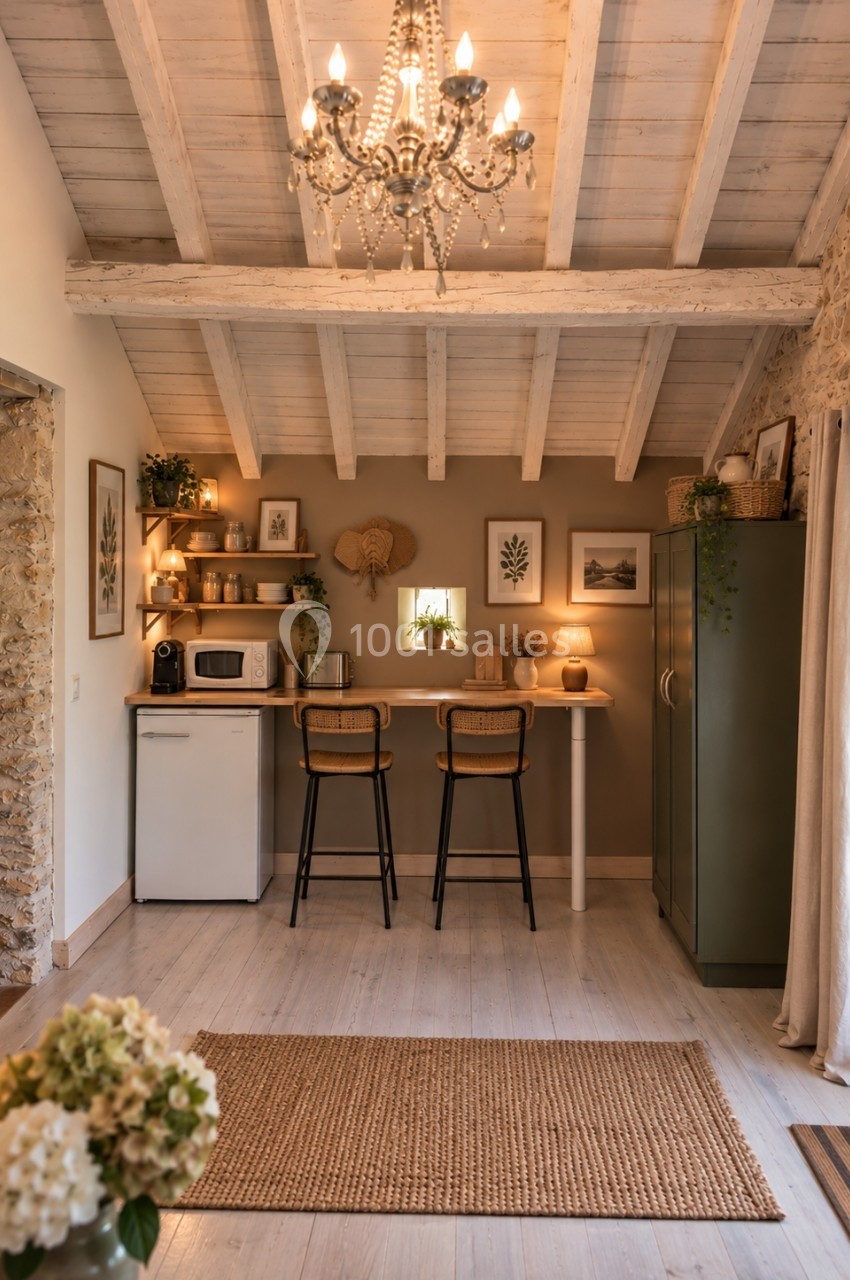 Cuisine compacte et chaleureuse avec poutres apparentes, étagères décorées, bar avec tabourets et éclairage doux.