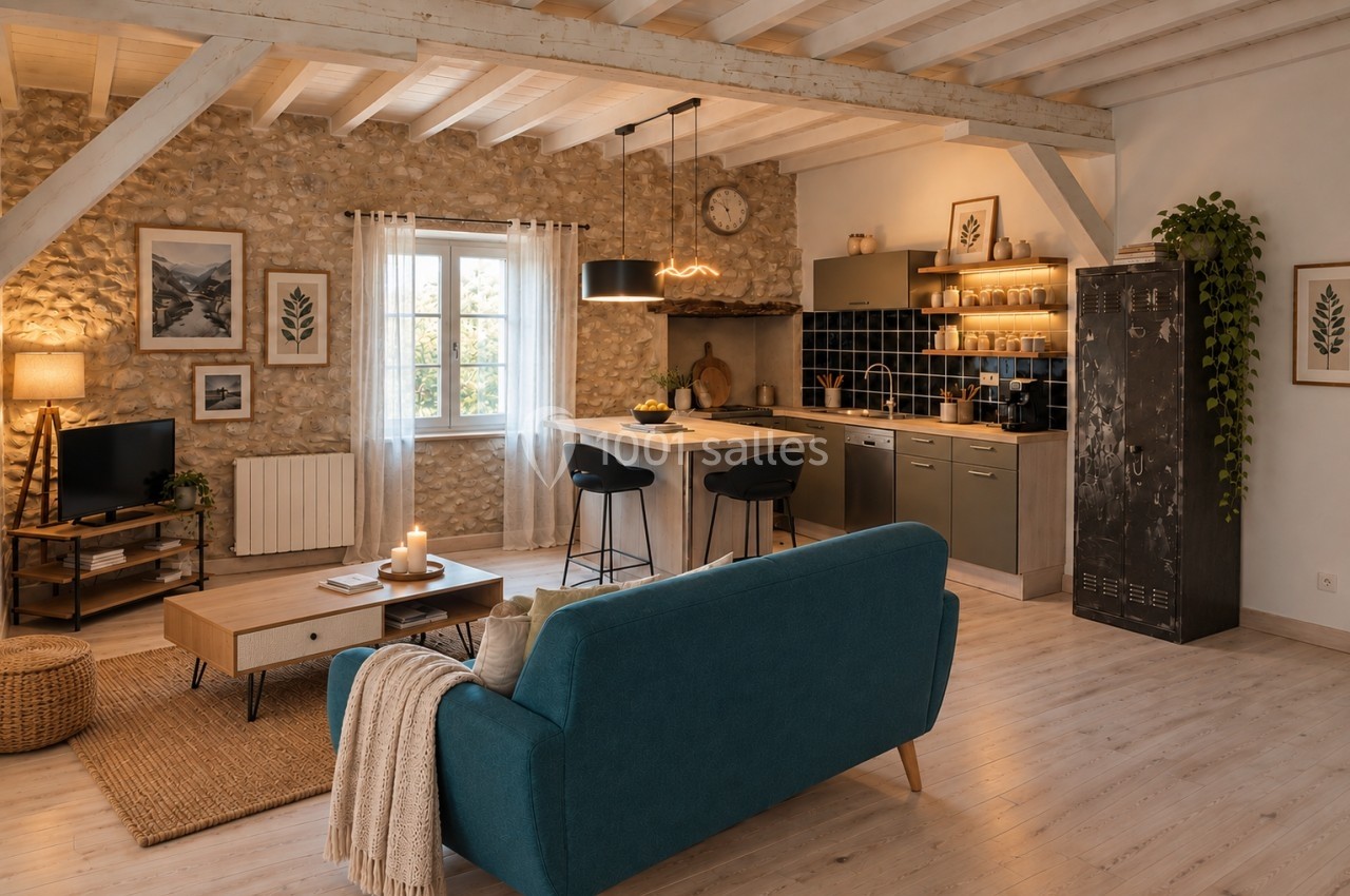 Salon ouvert avec canapé bleu, table basse en bois, cuisine équipée moderne et mur en pierre apparente.