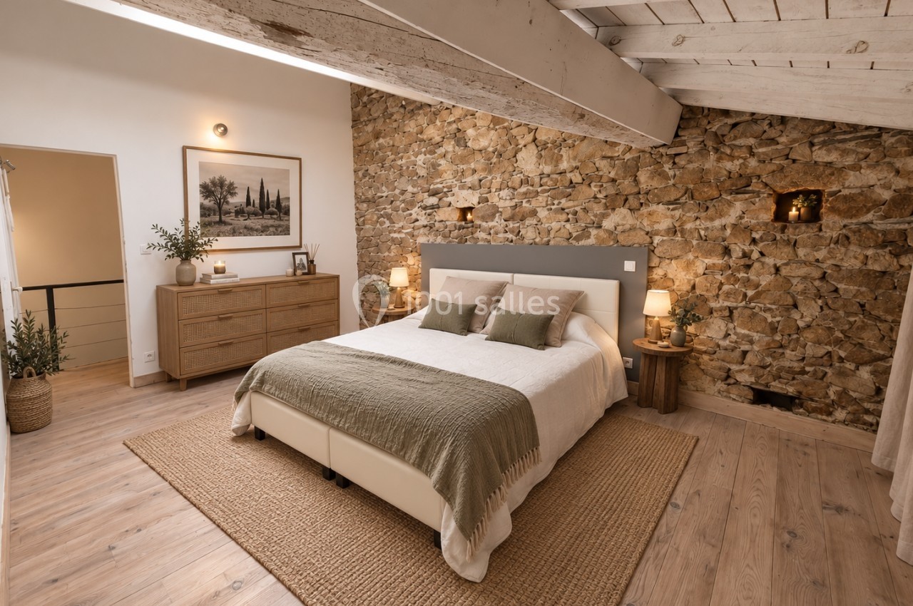 Chambre lumineuse avec lit double, mur en pierre, plafond avec poutres apparentes et mobilier en bois clair.