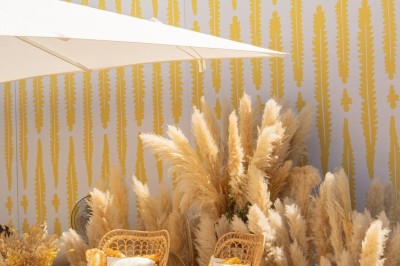 Miniature J&b Event #12 Chaises en rotin entourées de pampas et de décorations jaunes, sous un parasol blanc dans un cadre lumineux.