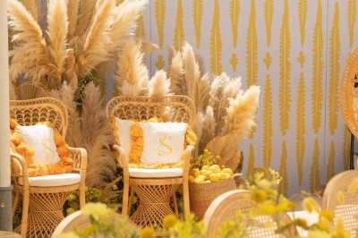 Miniature J&b Event #20 Chaises en rotin entourées de pampas et de décorations jaunes, sous un parasol blanc dans un cadre lumineux.