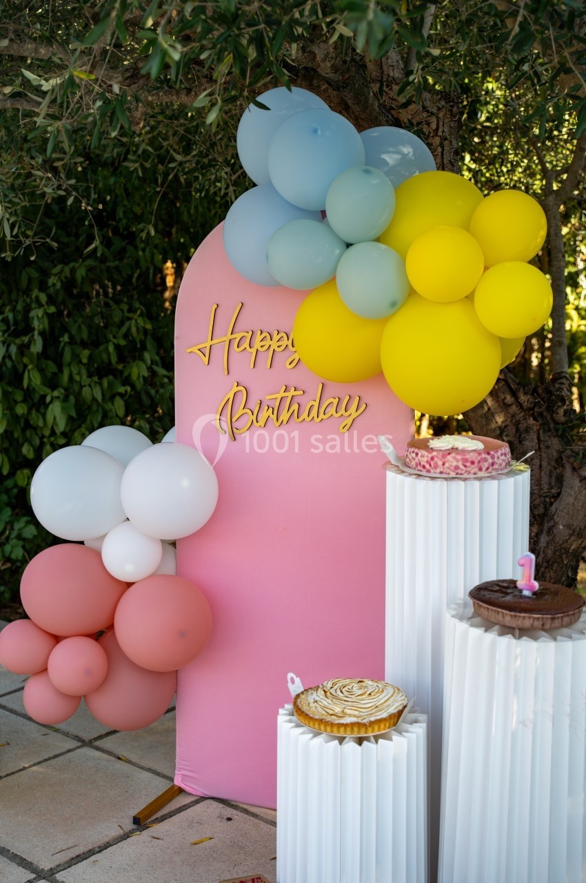 Décoration d'anniversaire en extérieur avec ballons colorés, panneau rose ’Happy Birthday’ et gâteaux sur des colonnes…