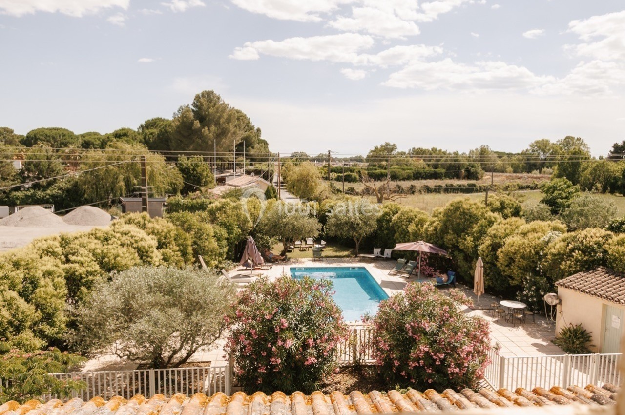 Vue d'une piscine entourée de végétation luxuriante et de terrasses aménagées sous un ciel partiellement nuageux.