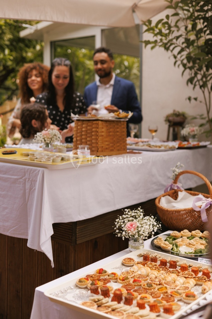 Buffet en plein air avec des amuse-bouches variés sur des tables, des invités discutant en arrière-plan.